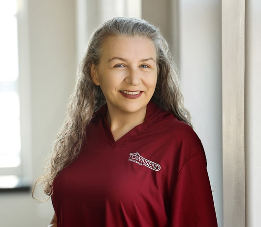 Smiling person in a maroon polo shirt standing by a bright window
