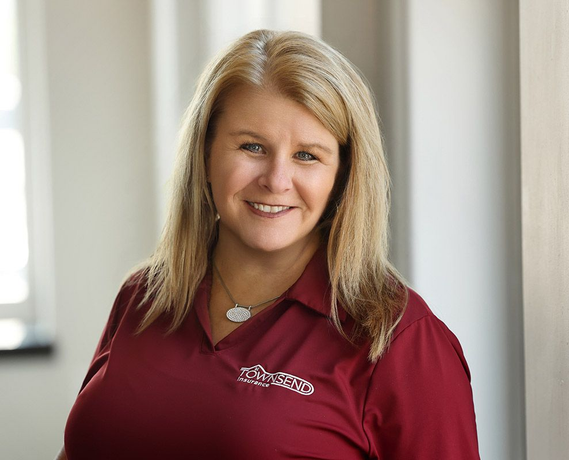 Smiling woman in a maroon polo standing indoors near a window