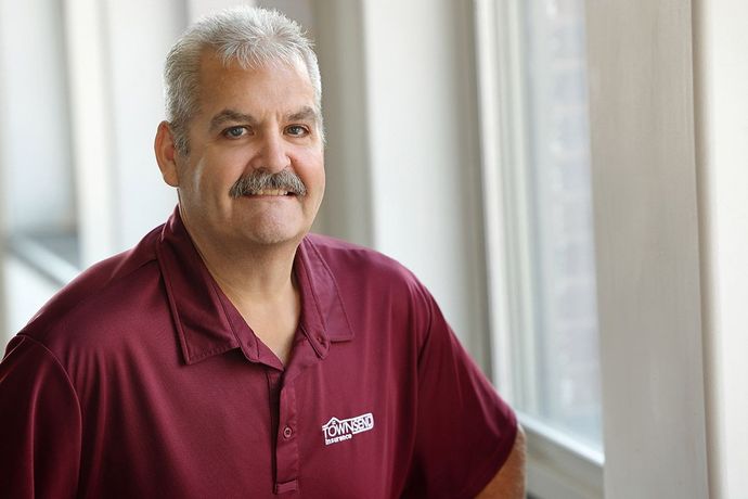 Man in a maroon polo shirt smiling beside a bright window