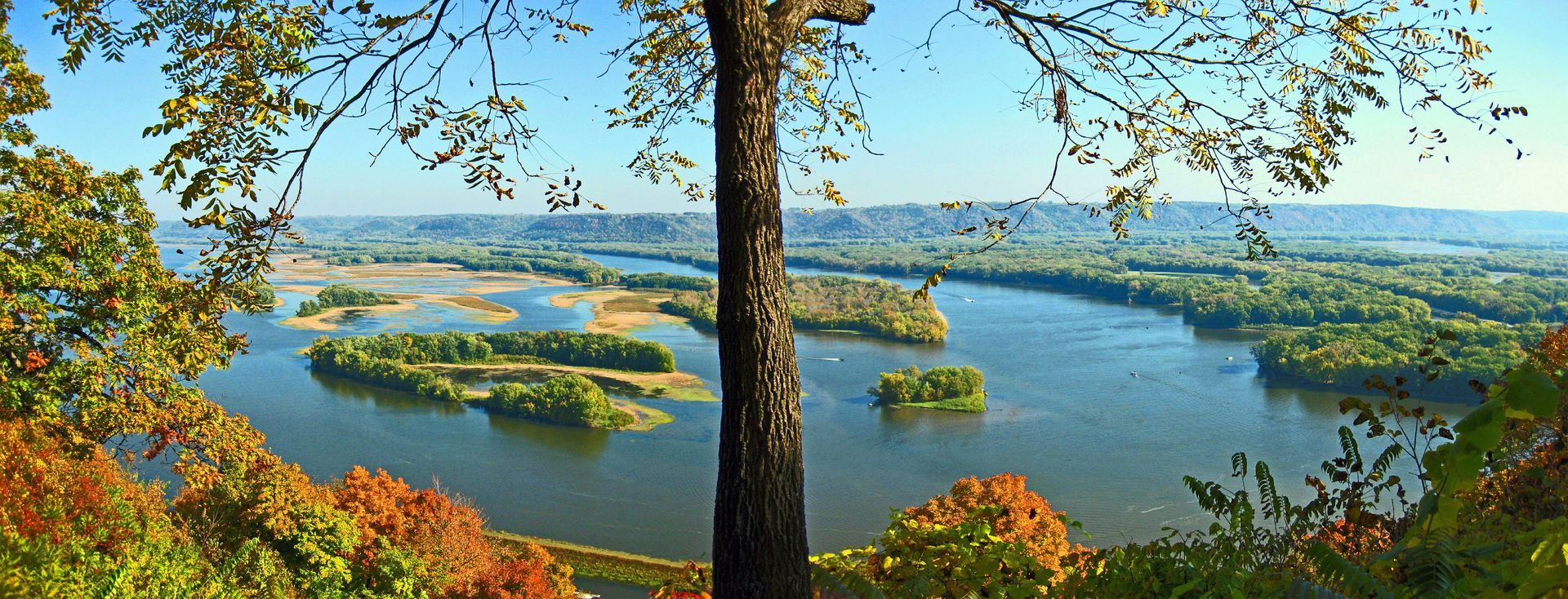 Scenic river valley with blue water, green islands, and autumn trees in the foreground.