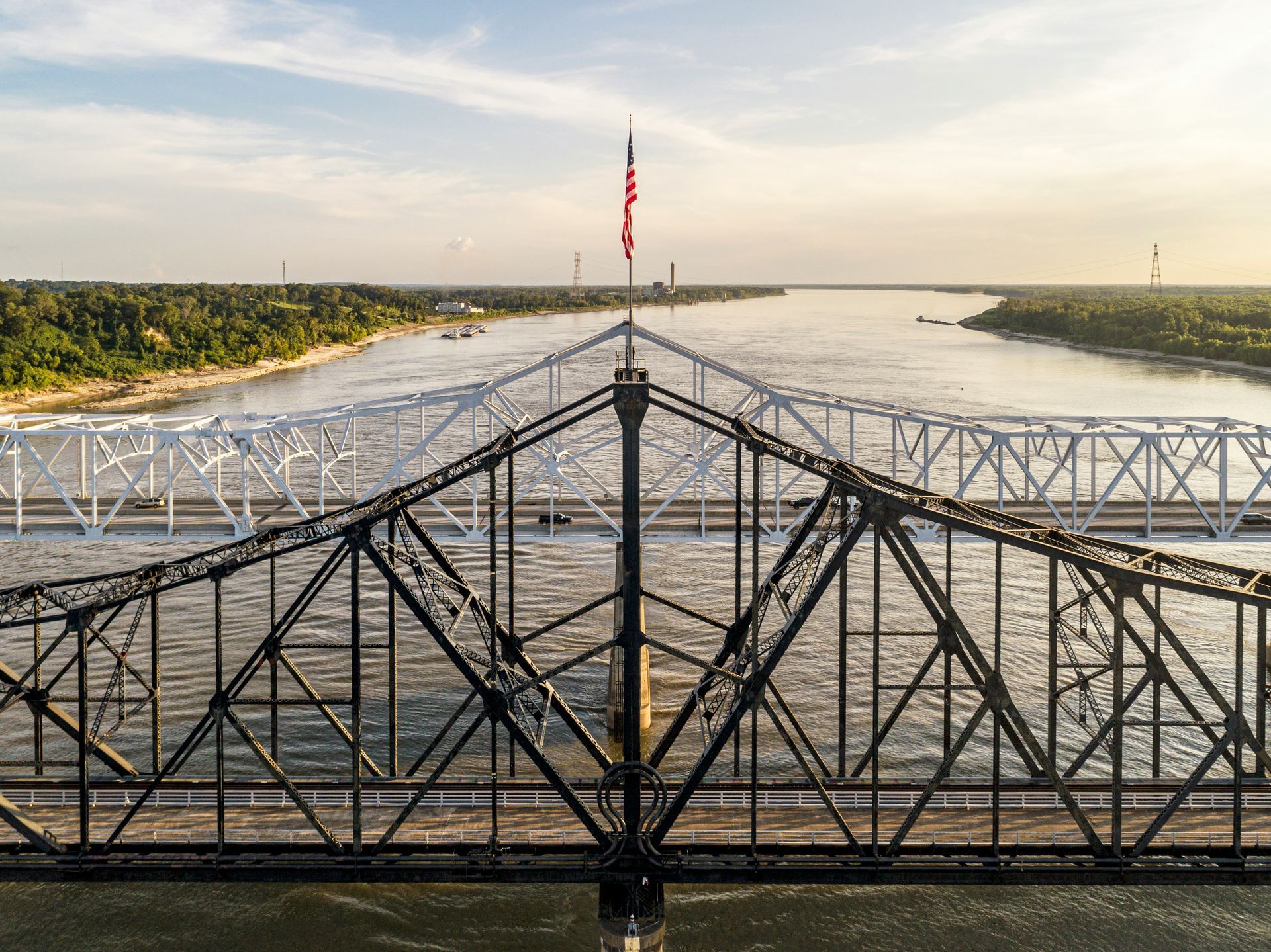 Bridge over a river at sunset, with a red flag on a central pole and green banks on both sides