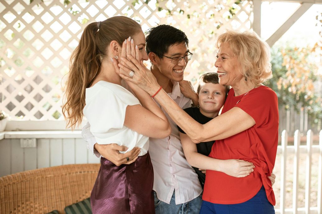 Two adults and a child smiling and hugging on a porch with a white lattice backdrop