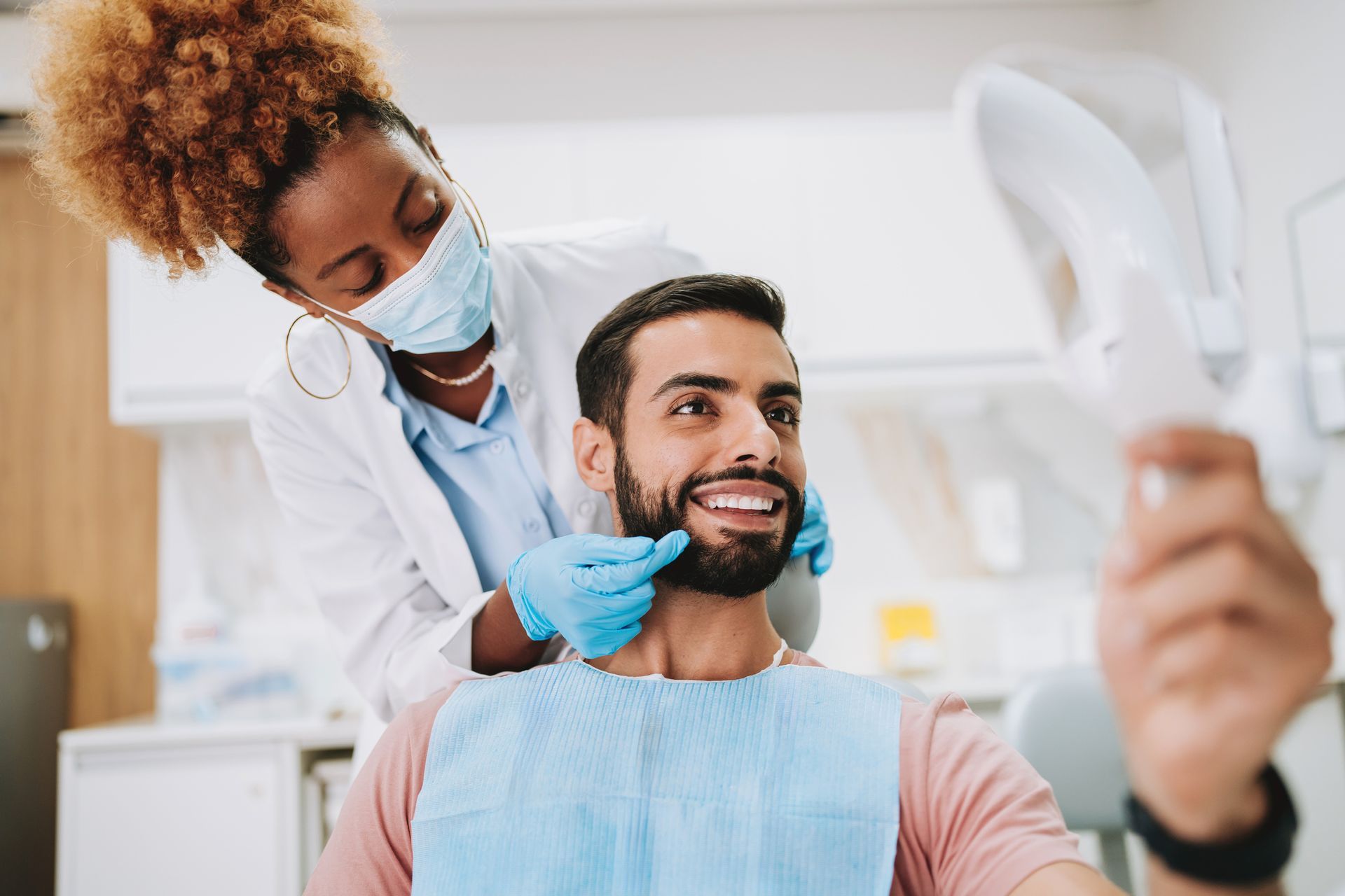 Dentist and patient in dental office. Dentist in mask and gloves examines patient's teeth with mirror.