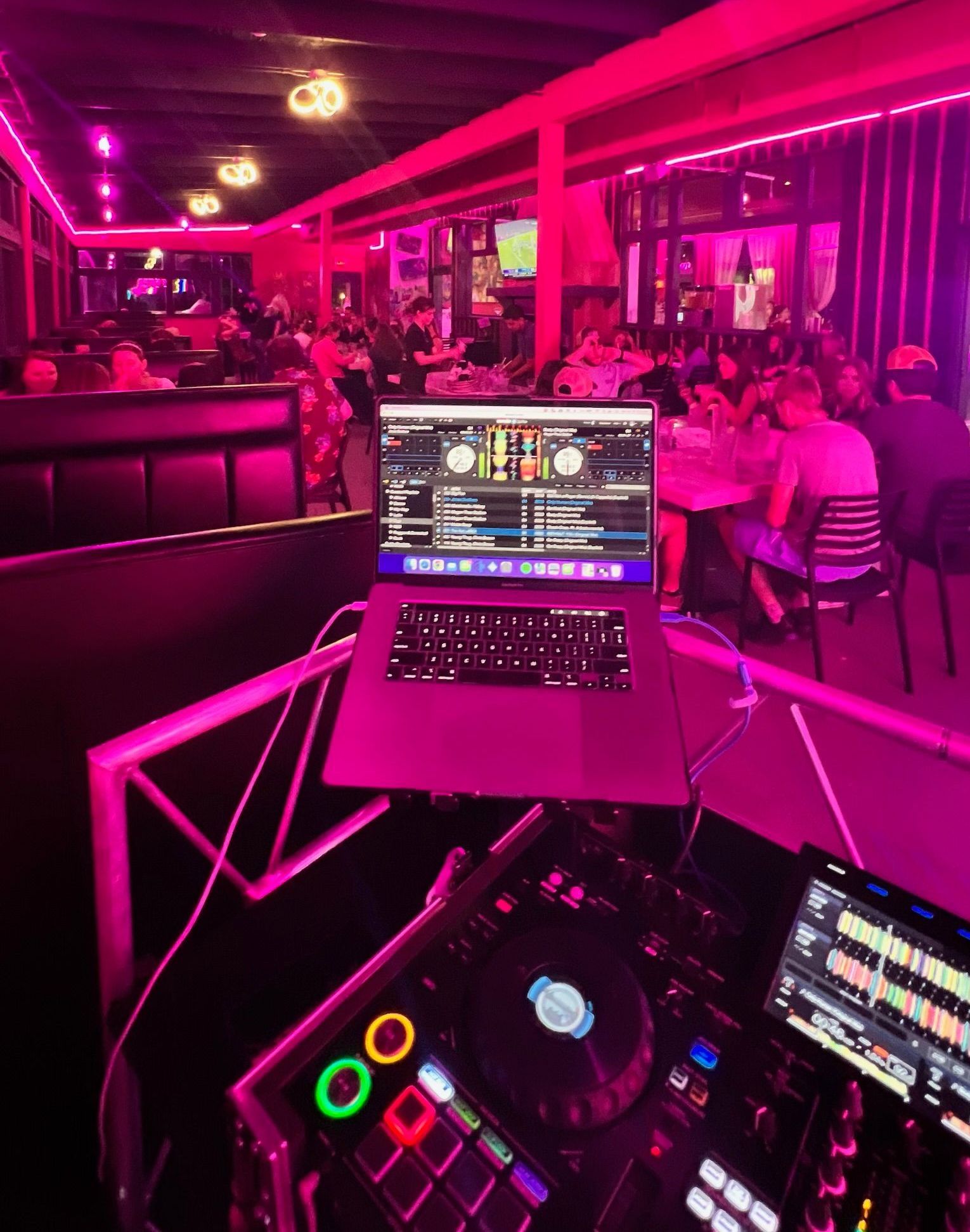 DJ booth overlooking a neon-pink lit nightclub with people seated at tables