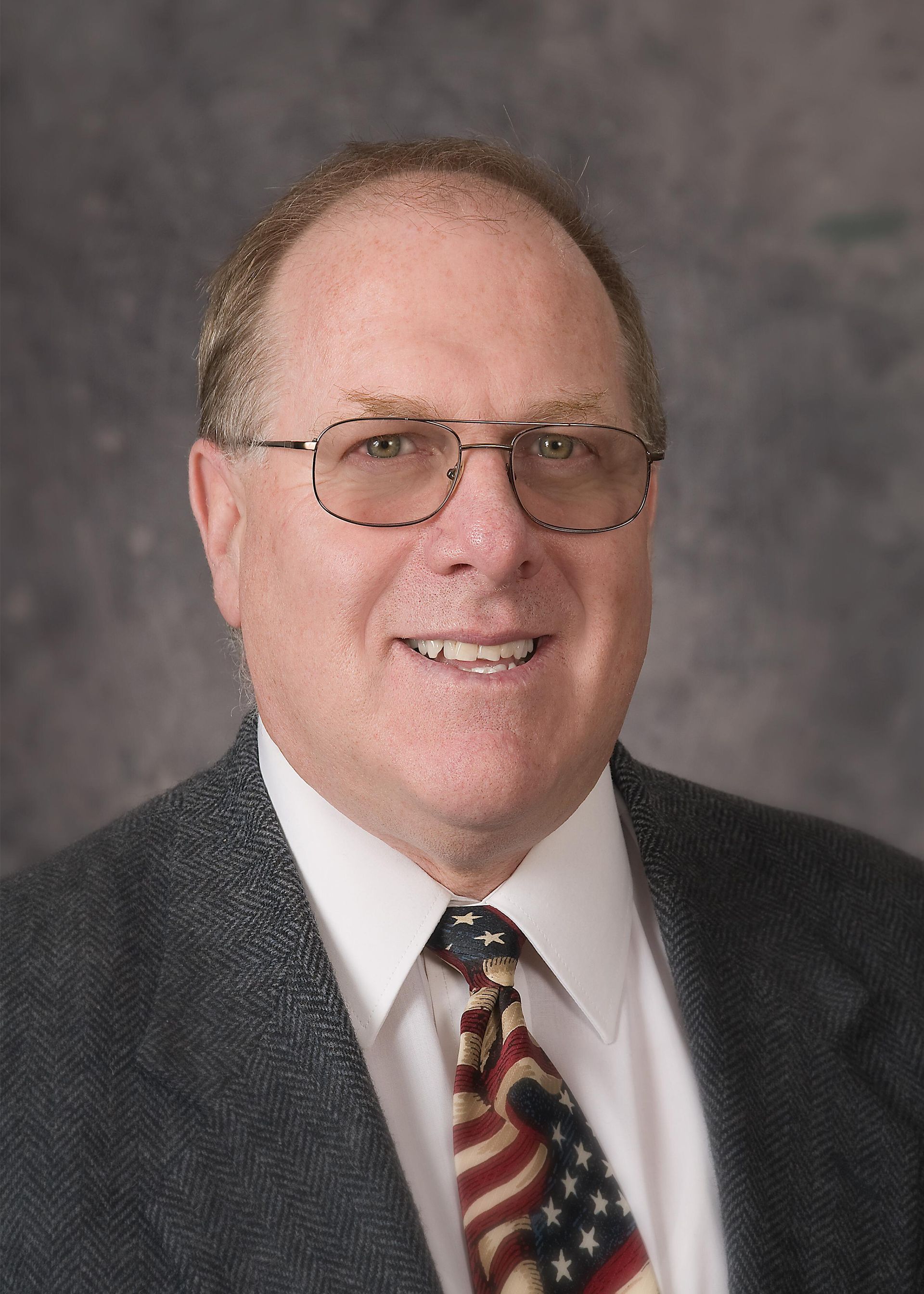Portrait of a man in a suit and patterned tie against a gray studio backdrop