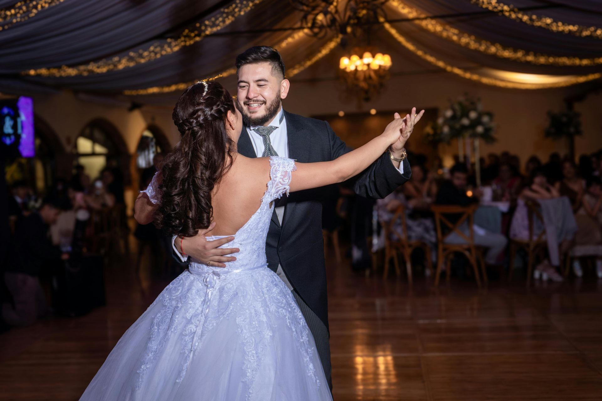 Bride and groom dancing at a wedding reception; she wears a white dress, he a black suit.