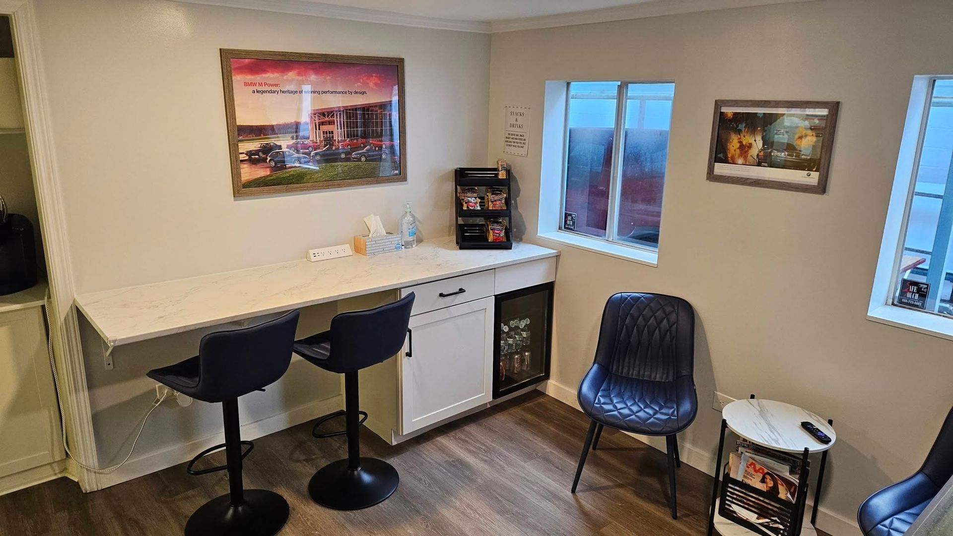Small home office with a white desk, two stools, chair, wall art, and windows. | Tony's European Auto Service