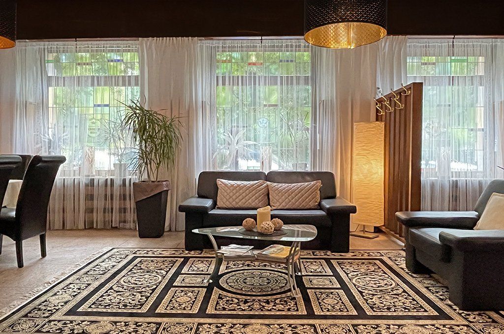 Lobby mit schwarzem Sofa, gemustertem Teppich und transparenten Vorhängen.