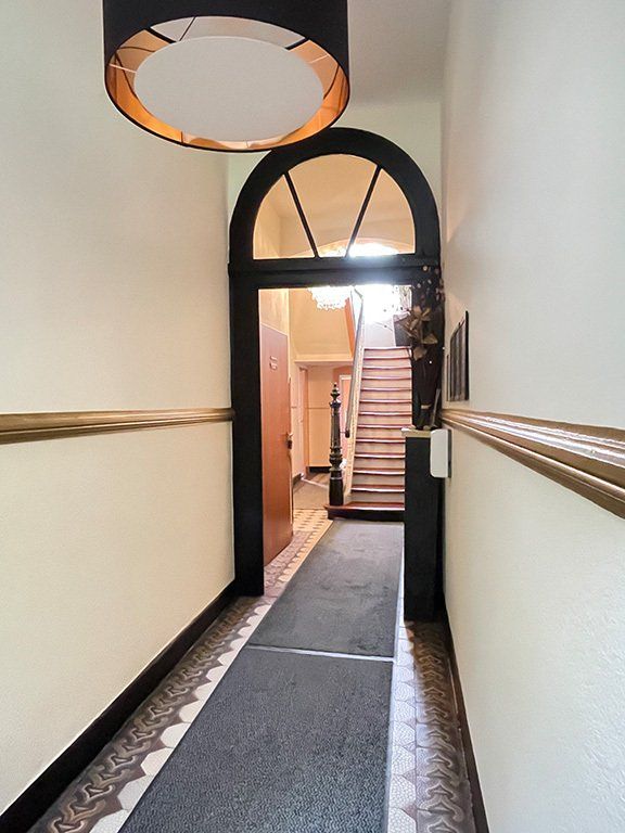 Flur mit Bogentür, Treppe im Hintergrund, gemusterten Bodenfliesen und schwarz-goldenen Details.