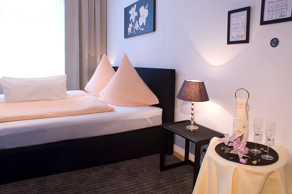 Schlafzimmer mit Einzelbett, Tisch mit Lampe und Getränken, Weltkartenbild.