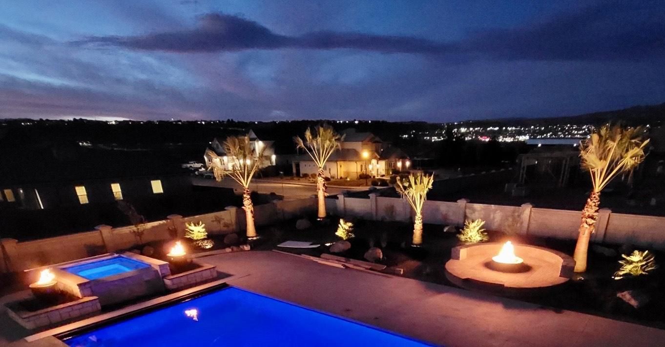 An aerial view of a swimming pool at night with a fire pit and palm trees.