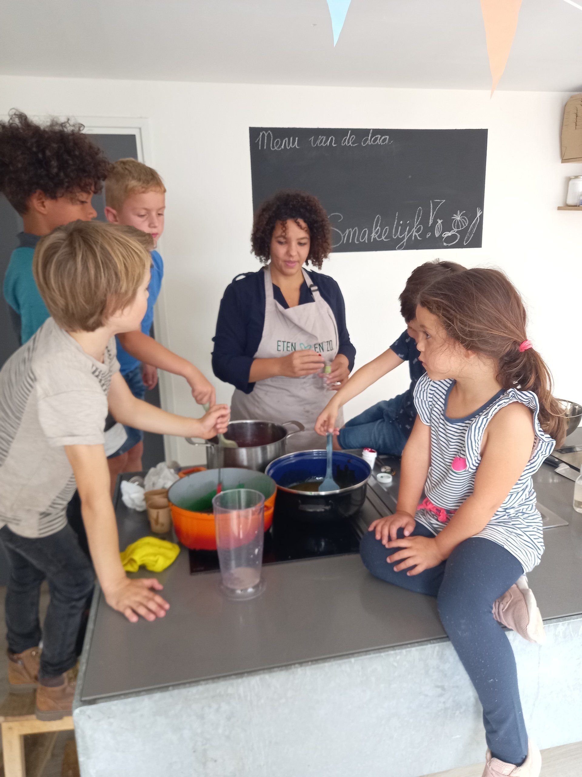 Een groep kinderen en een instructeur werken samen rond een keukeneiland en roeren mengsels in kleurrijke kommen.