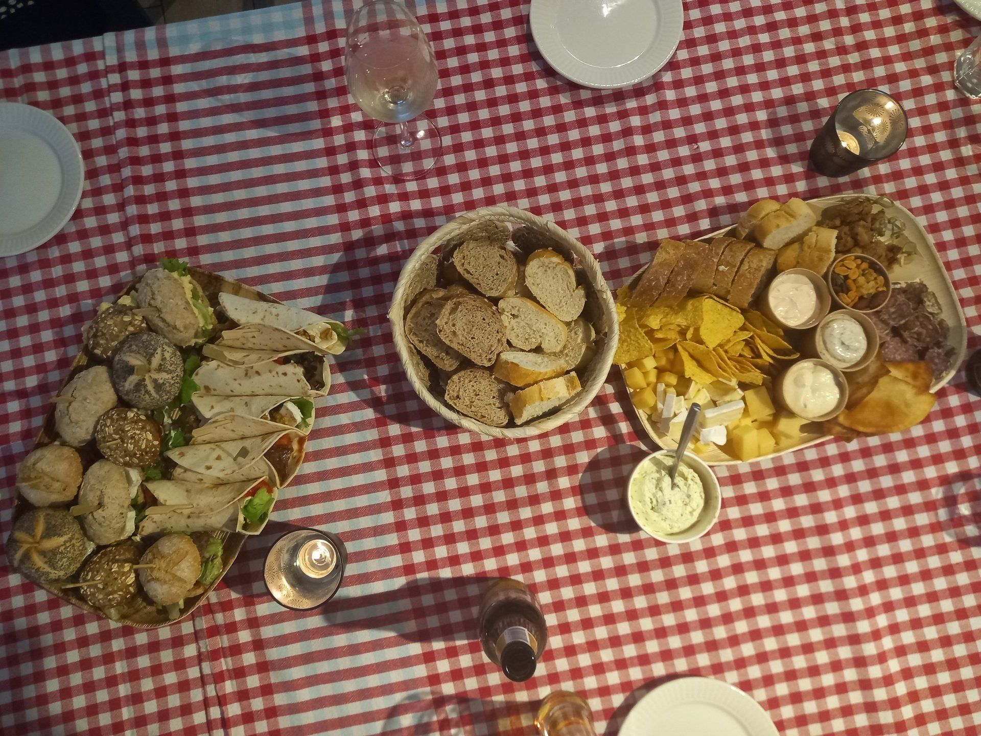 Een foto vanuit een hoog perspectief van een rood-wit geblokt tafelkleed met een schaal vol sandwiches, een kom brood en hapjes.