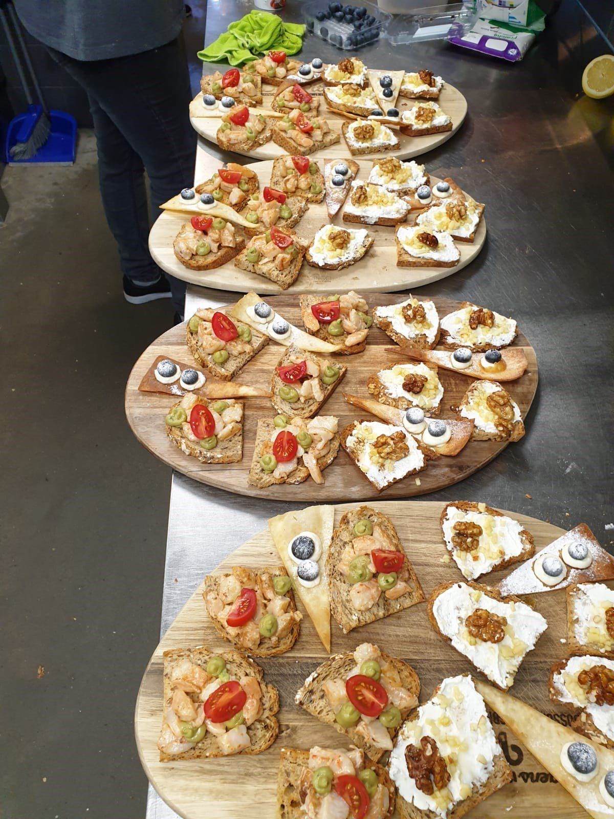 Vier houten schalen met diverse bruschetta- en crostini-hapjes, waaronder tomaat, roomkaas en walnoten.