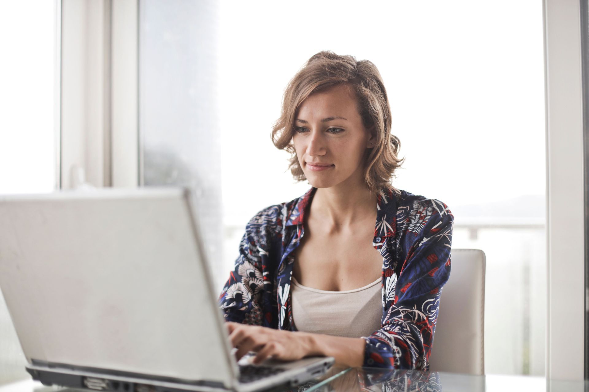 Woman typing on a laptop at a bright desk, looking focused.