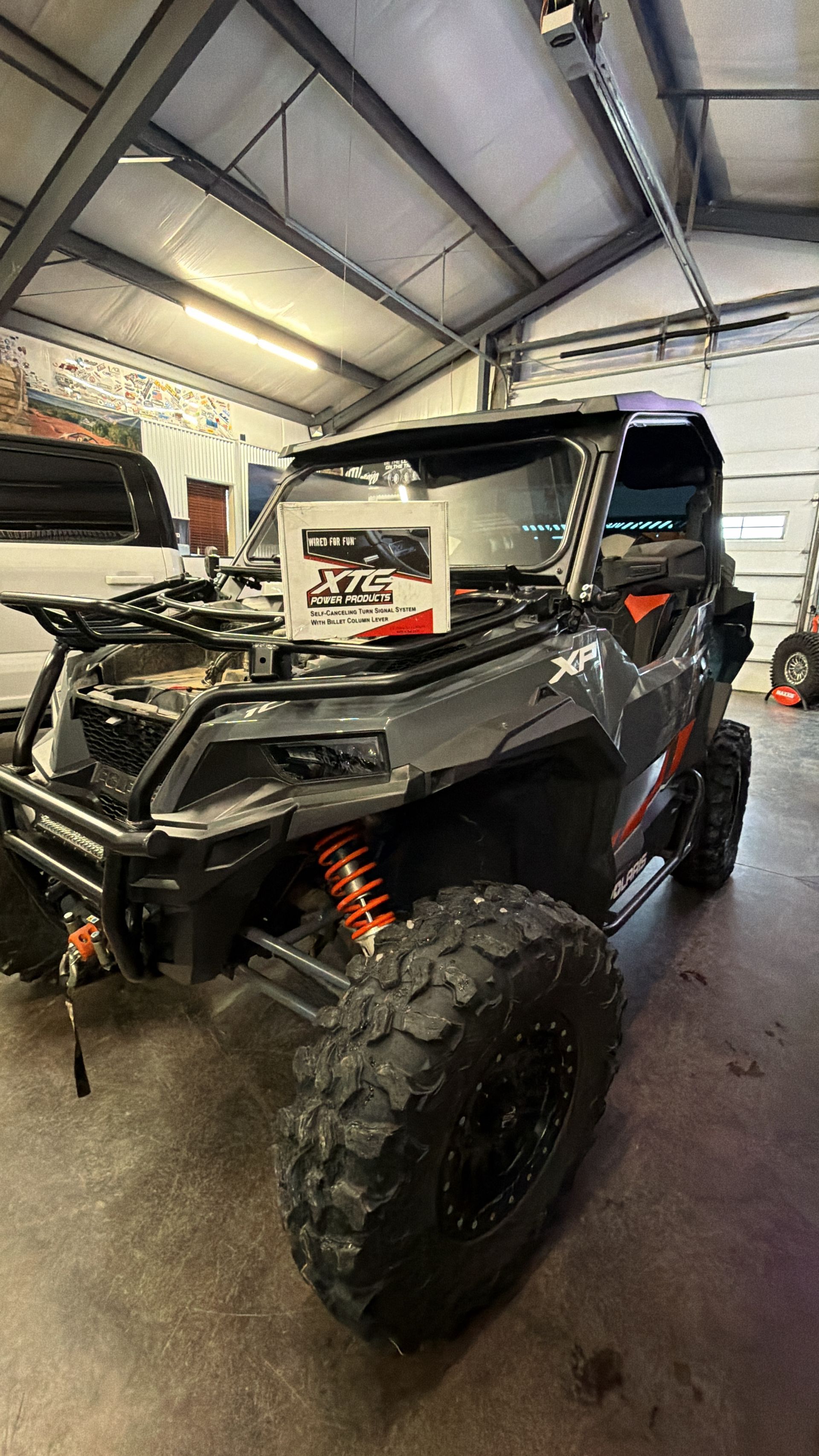 Black UTV with large tires in a garage, hood open and front bumper exposed.