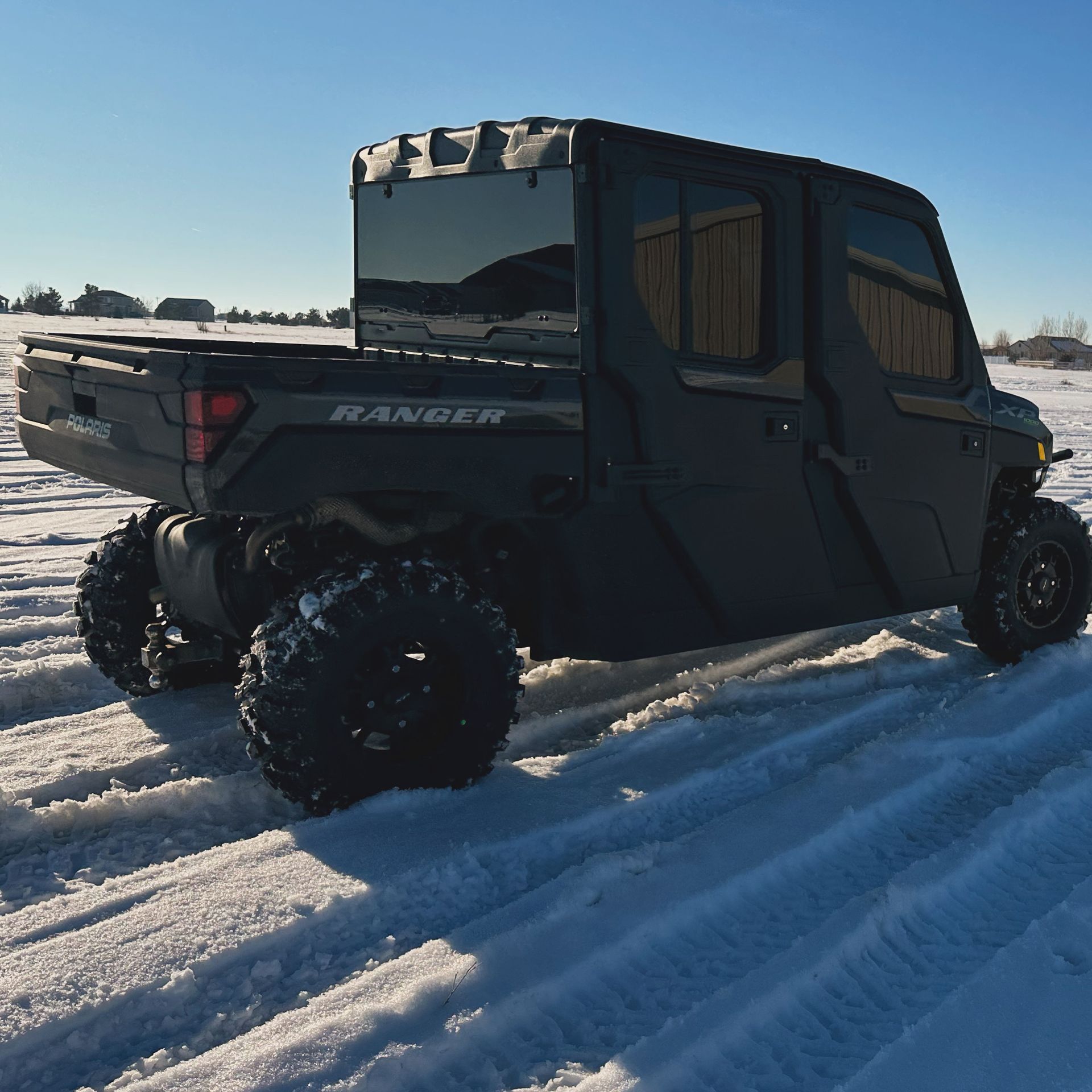 Black off-road utility vehicle with large tires driving on a snowy road in bright sunlight