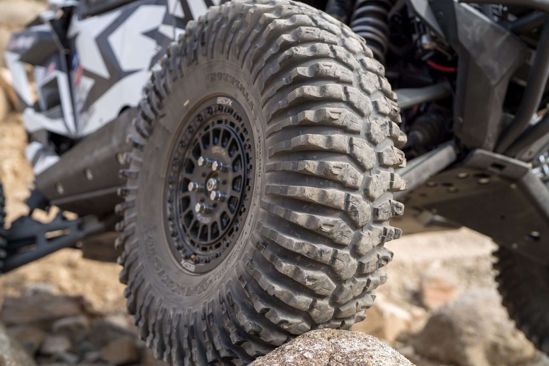 Close-up of a rugged off-road tire on a camouflaged vehicle driving over rocks