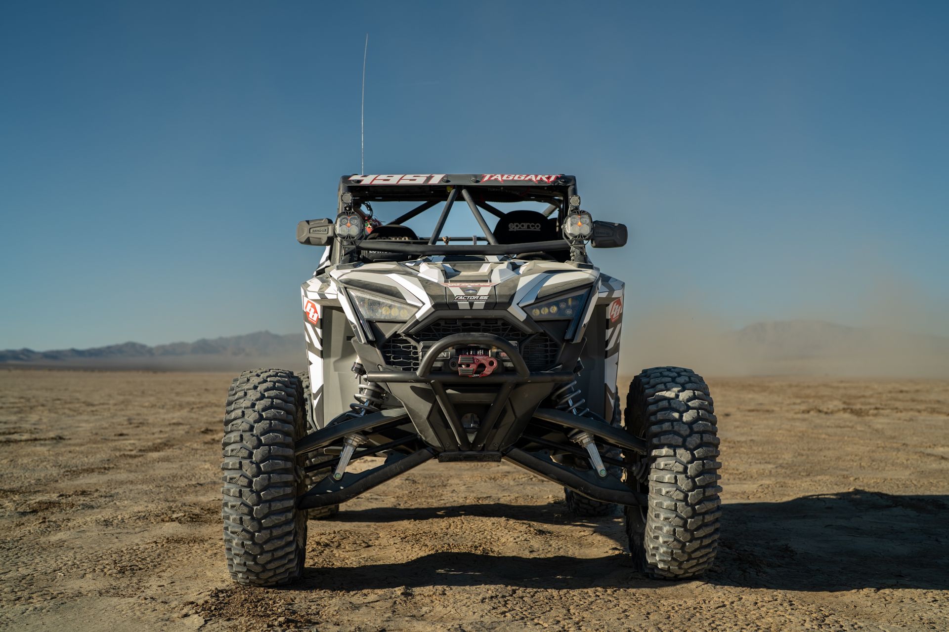 Off-road buggy with large tires on a dusty desert plain under a clear blue sky