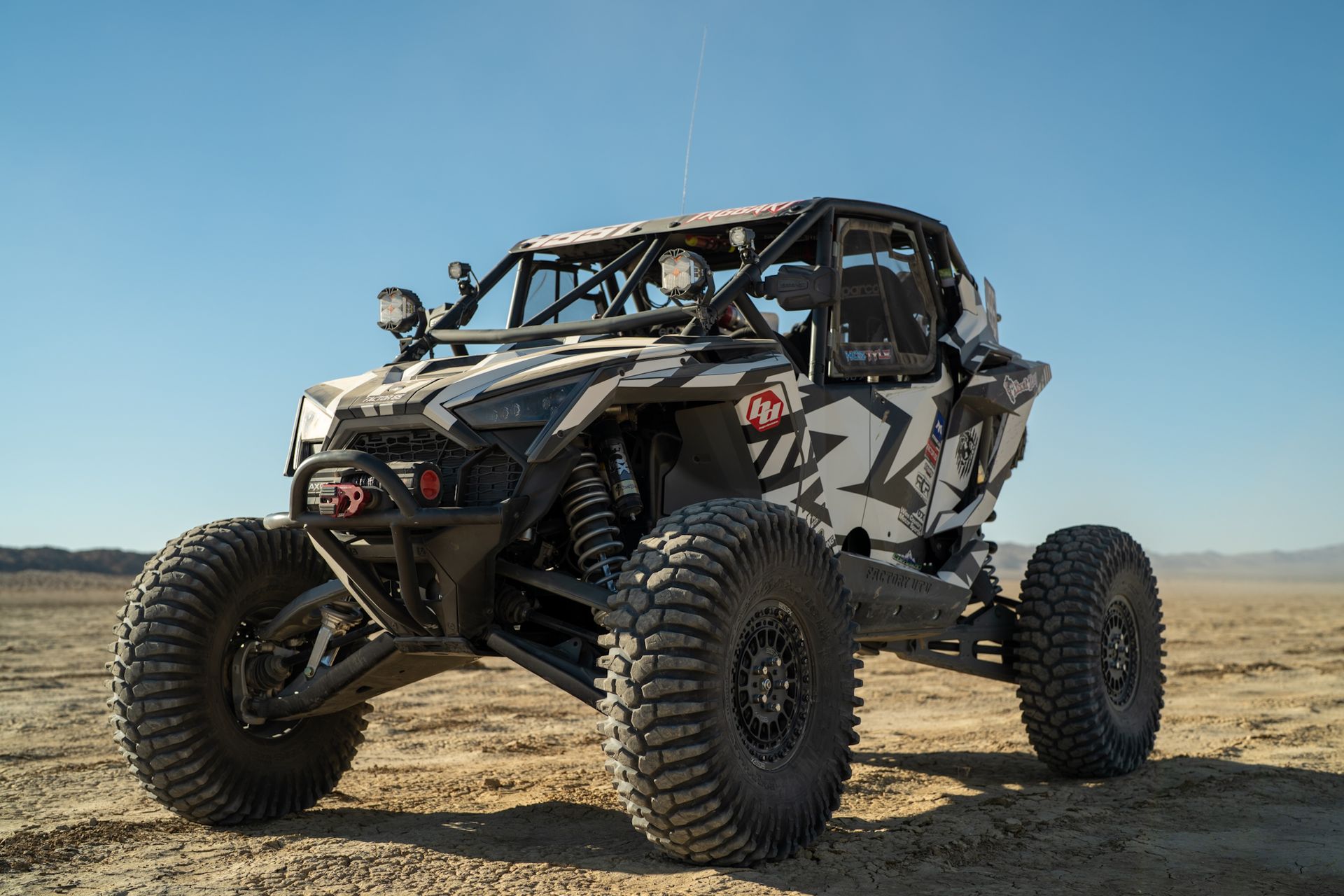 Off-road dune buggy with oversized tires parked on a dirt plain under a clear blue sky