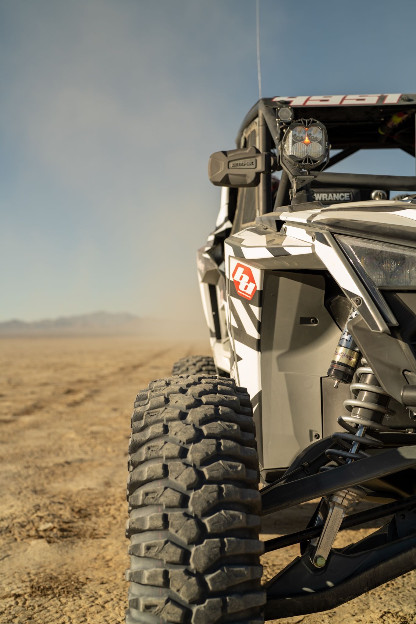 Off-road buggy tire on a dusty desert track, with vehicle body and suspension visible.