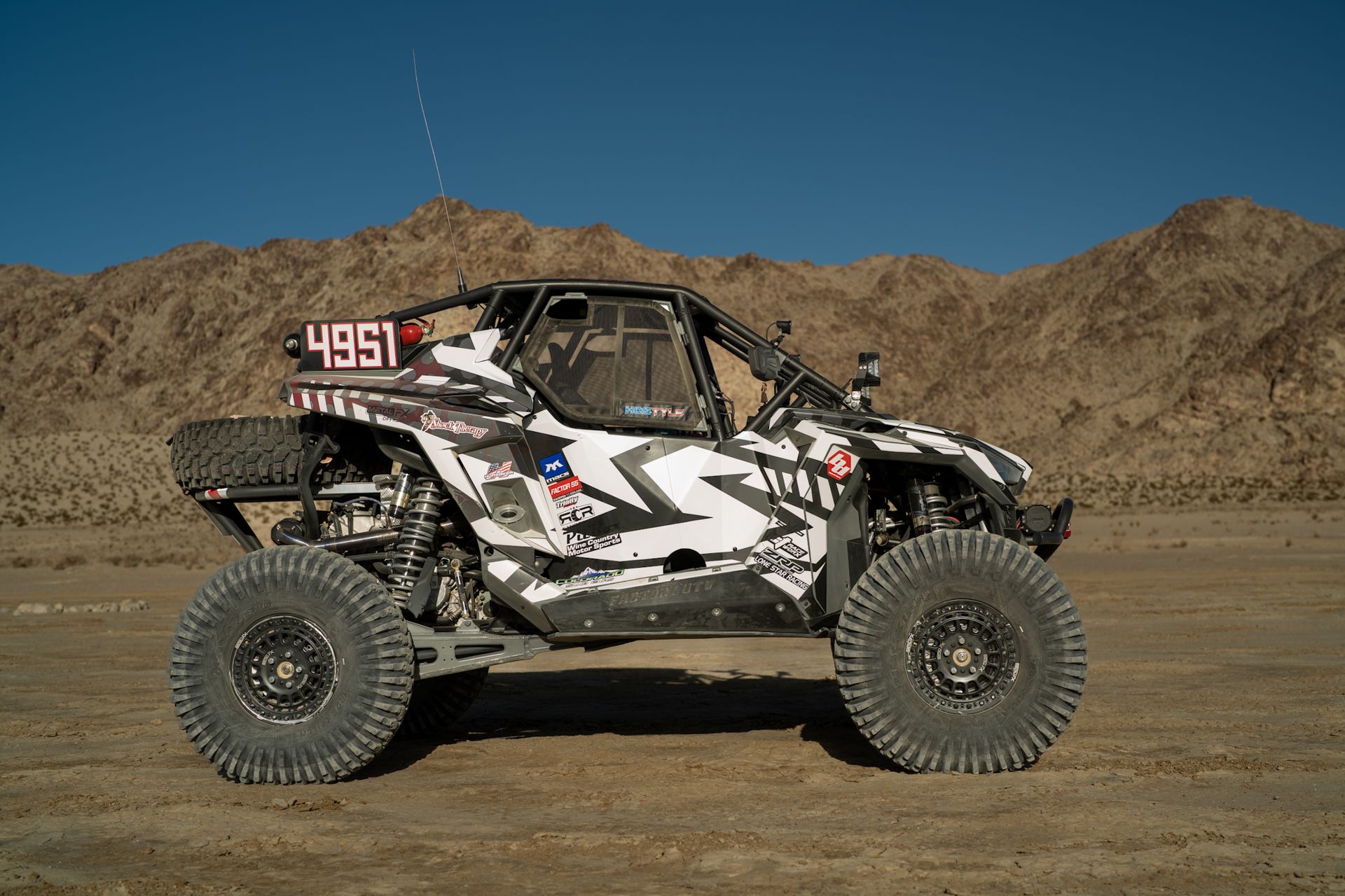 Off-road buggy with number 4851 racing across a dusty desert landscape with mountains in the background