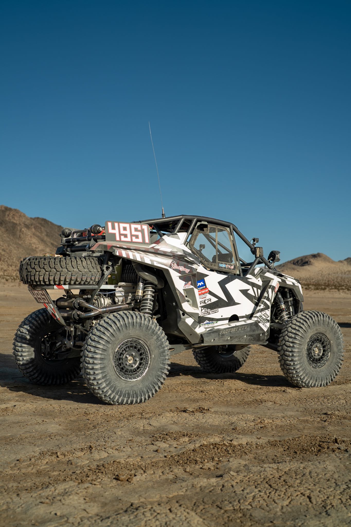 Off-road buggy with camouflage wrap driving on dirt in a desert landscape under a clear blue sky