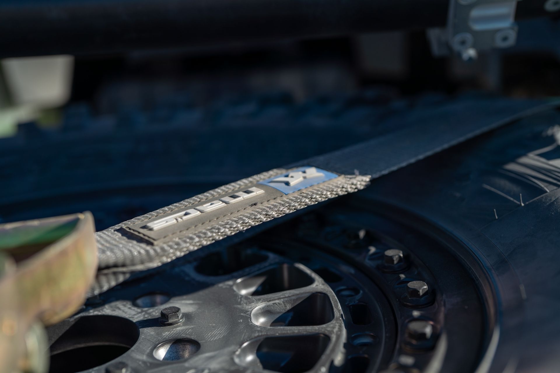 A close-up of a metallic tool on a dark mechanical surface, with a wheel or gear visible beside it.