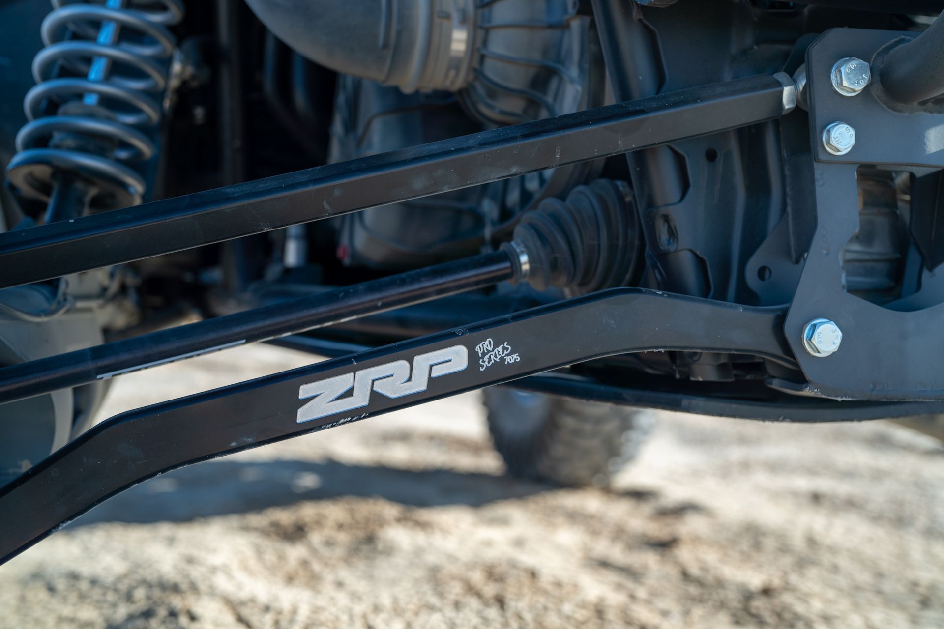 Close-up of a black vehicle suspension arm with ZRP logo and blue coil spring.