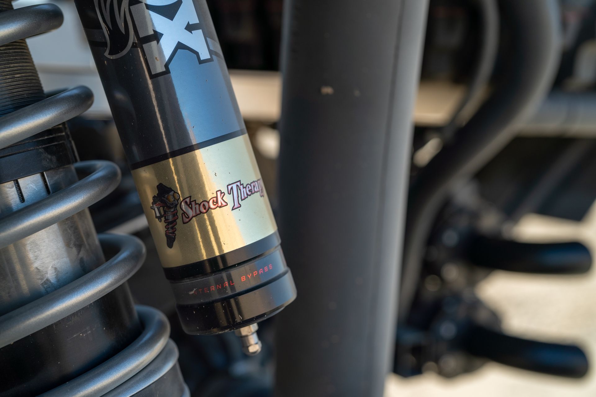 Close-up of a motorcycle suspension shock with a black and gold body and coil spring.