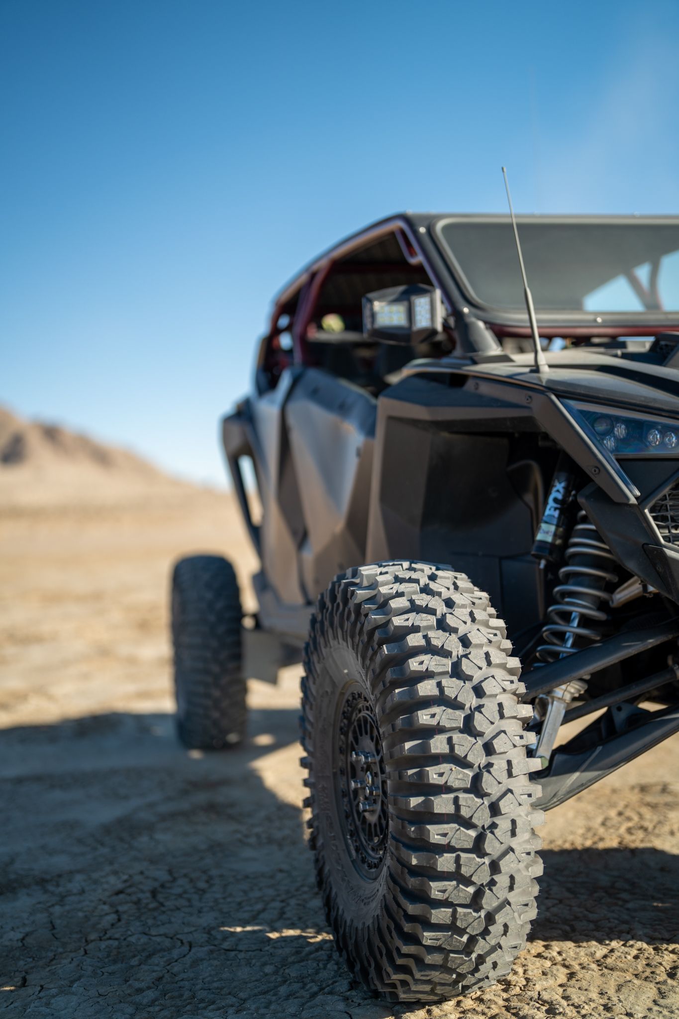 Black off-road buggy with large tires on a desert trail under a clear blue sky