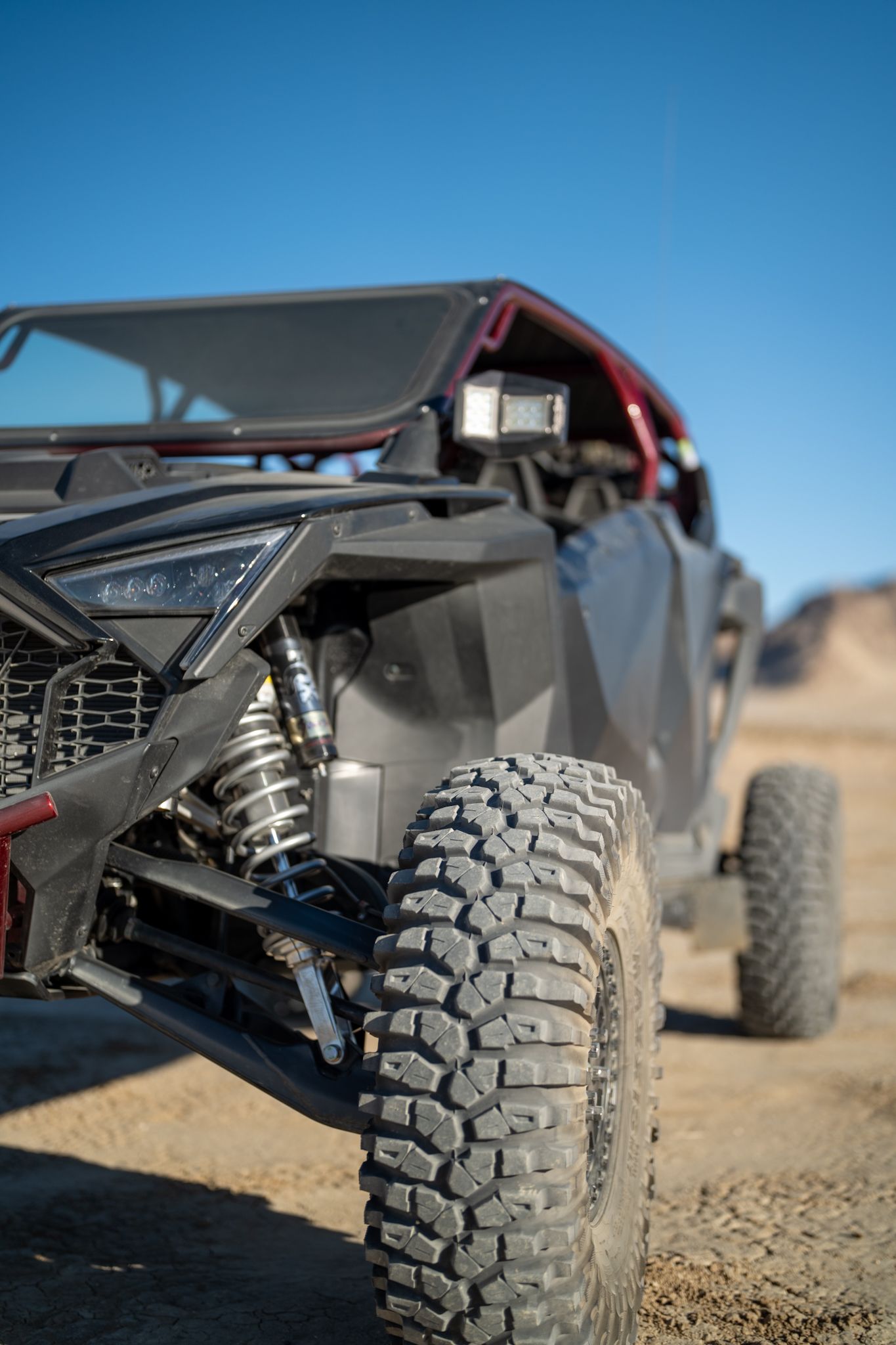 Off-road buggy with large tires driving on a dirt trail under a clear blue sky