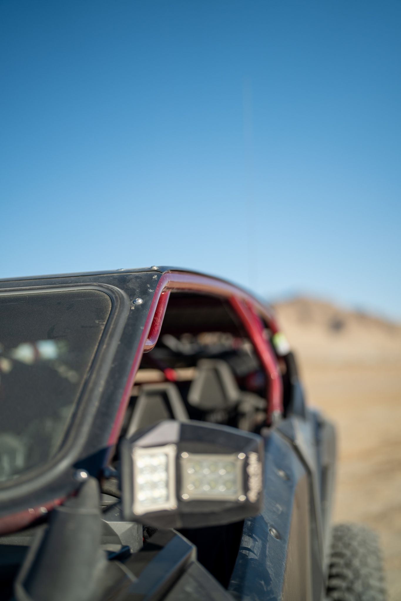 Off-road buggy close-up in desert, with red roll cage and large headlight under a clear blue sky