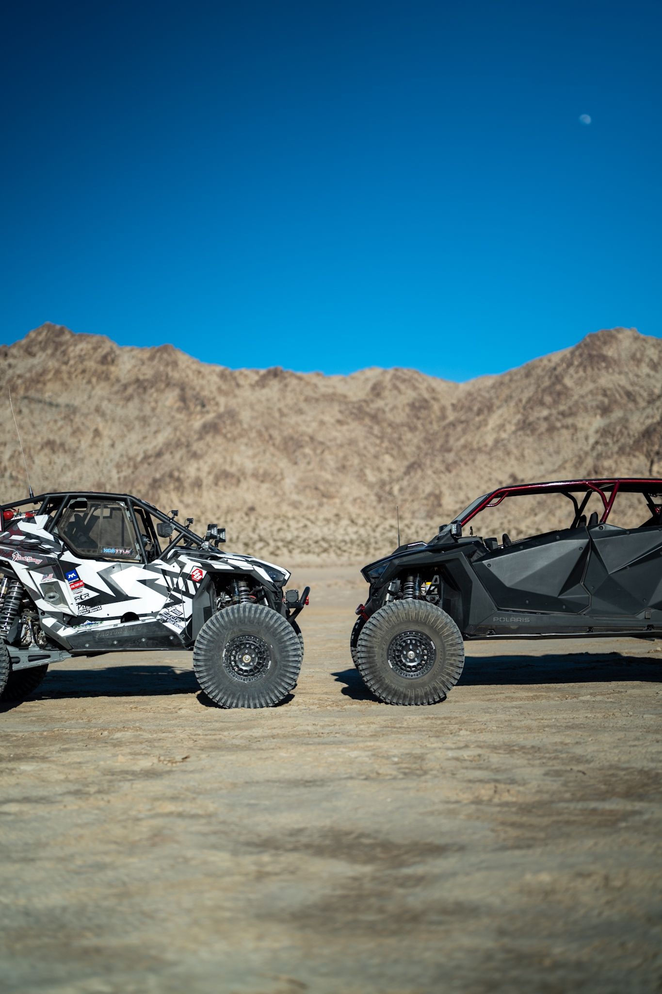 Two off-road dune buggies facing each other in a desert with mountains and blue sky.