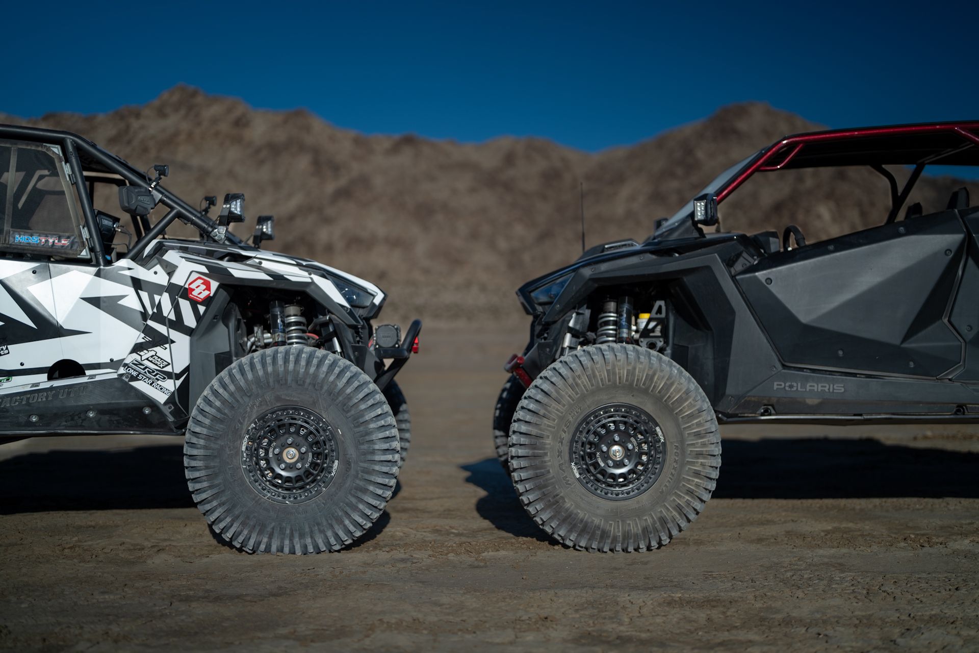 Two off-road side-by-side UTVs parked on dirt in a desert landscape
