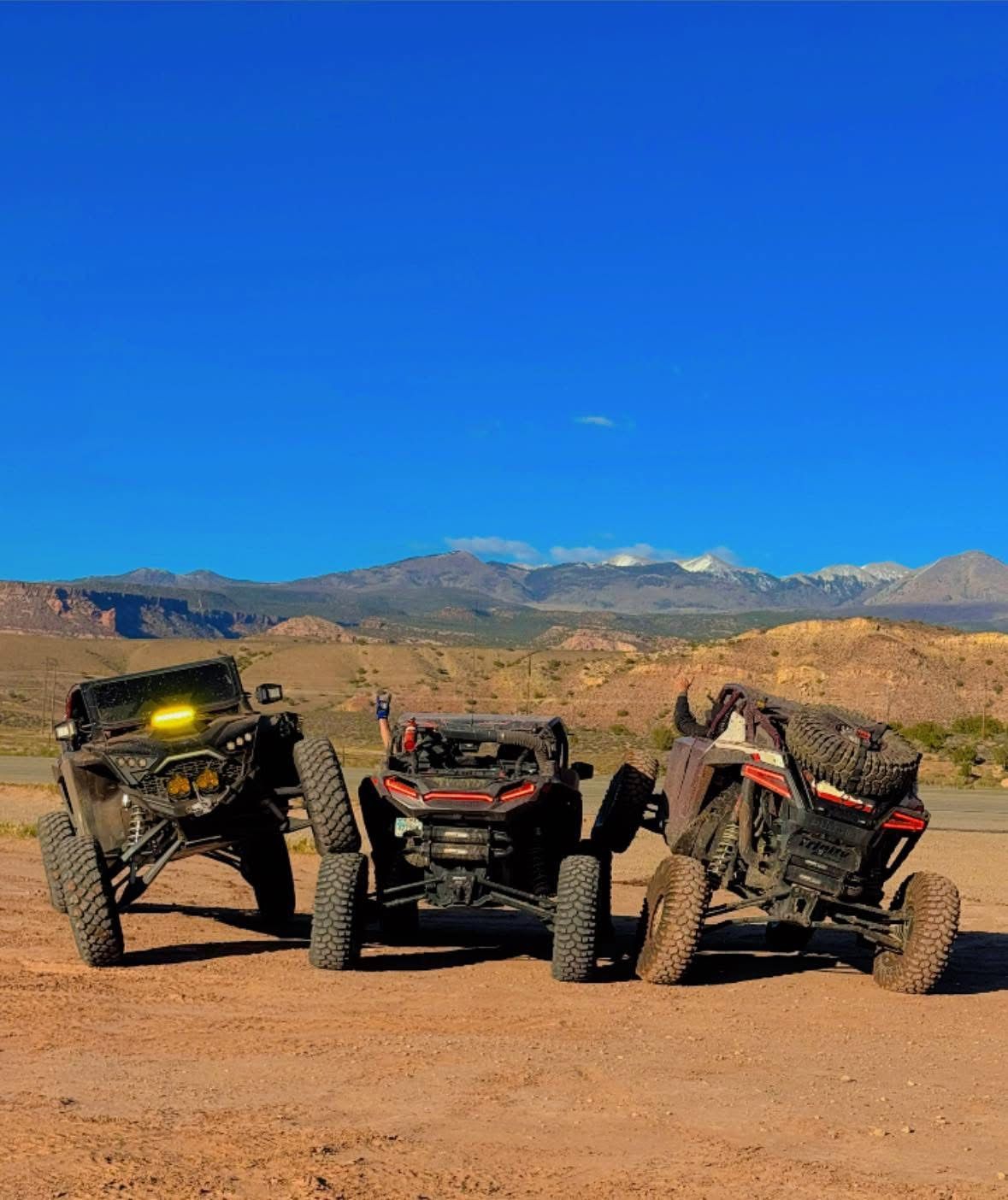 Three off-road dune buggies parked on a desert trail under a clear blue sky.
