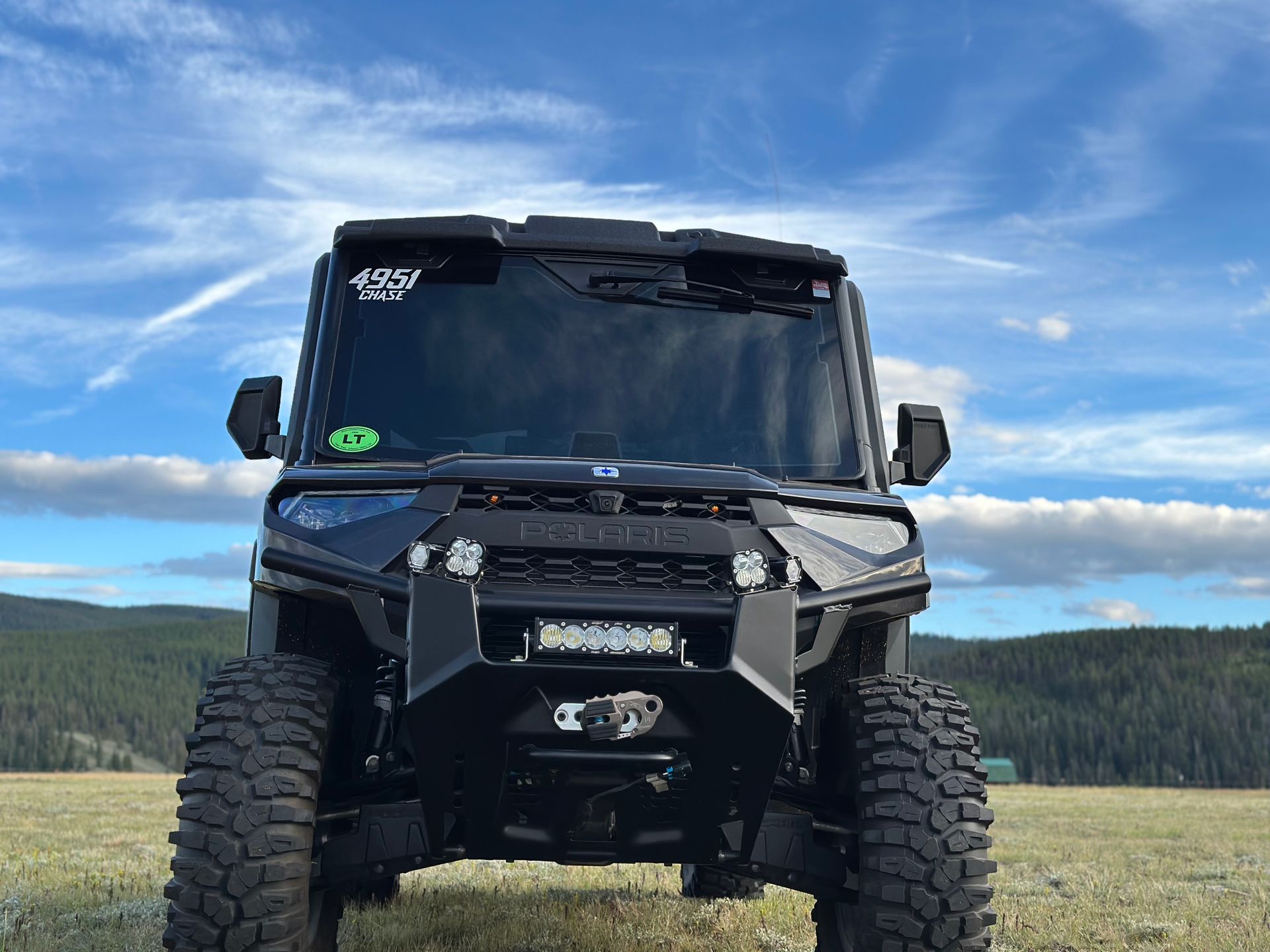 Black off-road truck with oversized tires parked in a grassy field under a blue sky