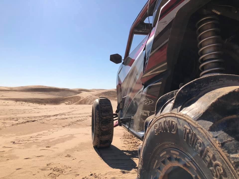 Off-road buggy tire in a sandy desert with dunes under a clear blue sky