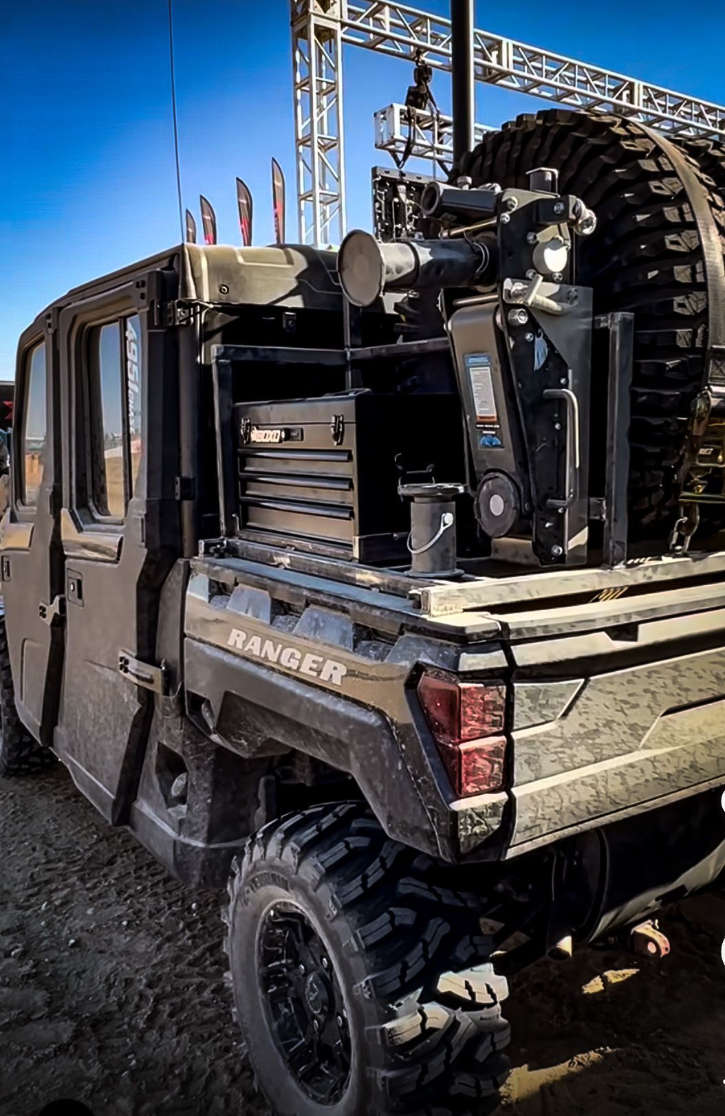 Black off-road Ranger pickup with oversized tires parked outdoors under a clear blue sky.