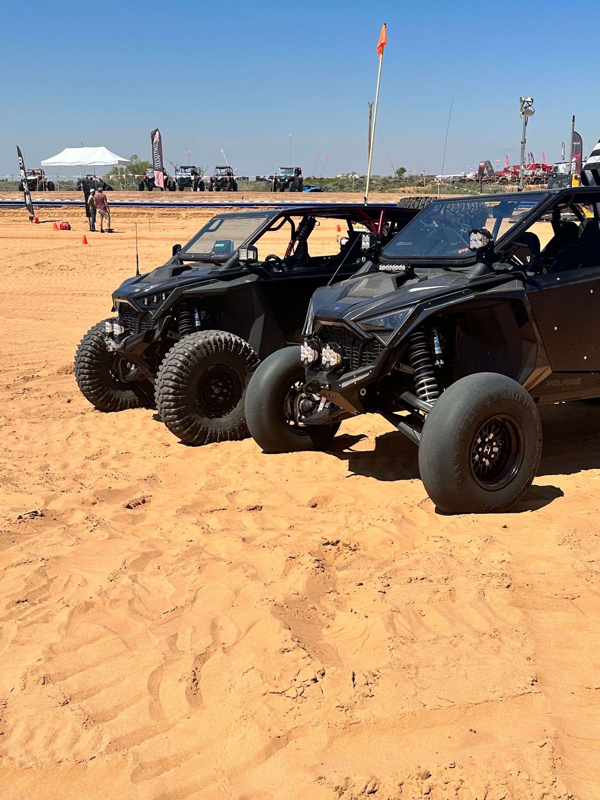 Two black off-road buggies parked on sandy terrain at an outdoor event