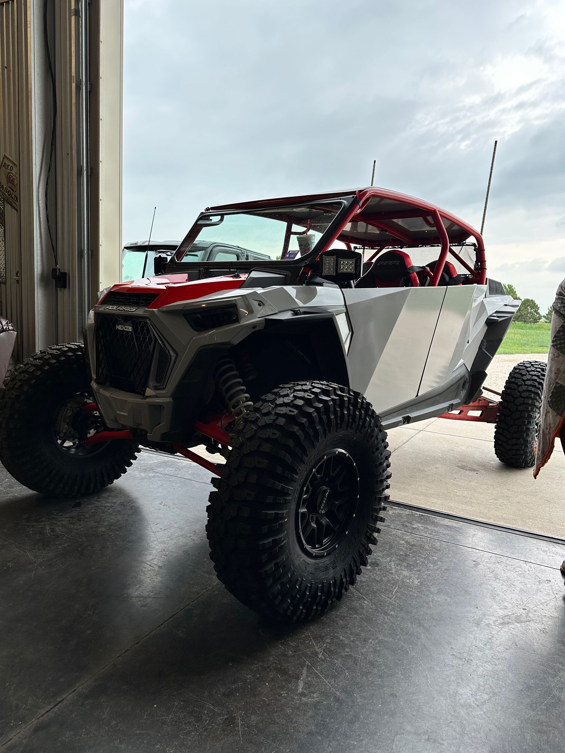 Off-road buggy with red roll cage and large tires parked in a garage doorway