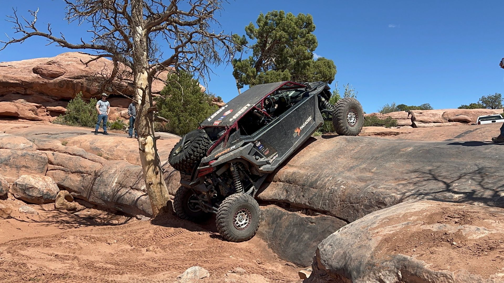 Off-road truck climbing a rocky desert ledge under a clear blue sky