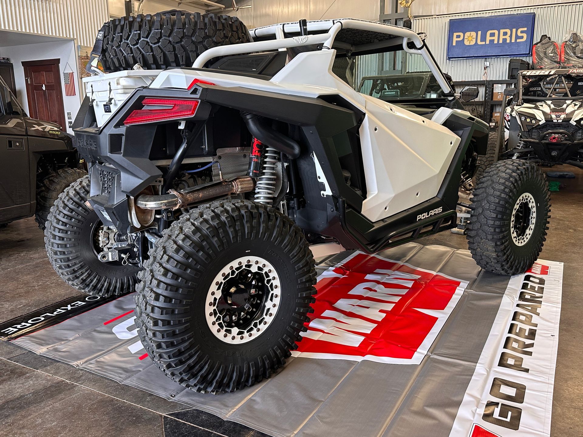 White Polaris off-road UTV with large tires displayed in a garage showroom