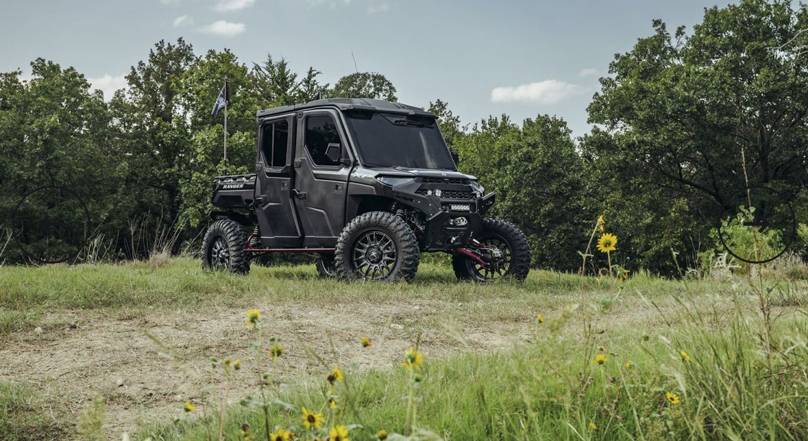 Black off-road truck driving through a grassy field with trees in the background