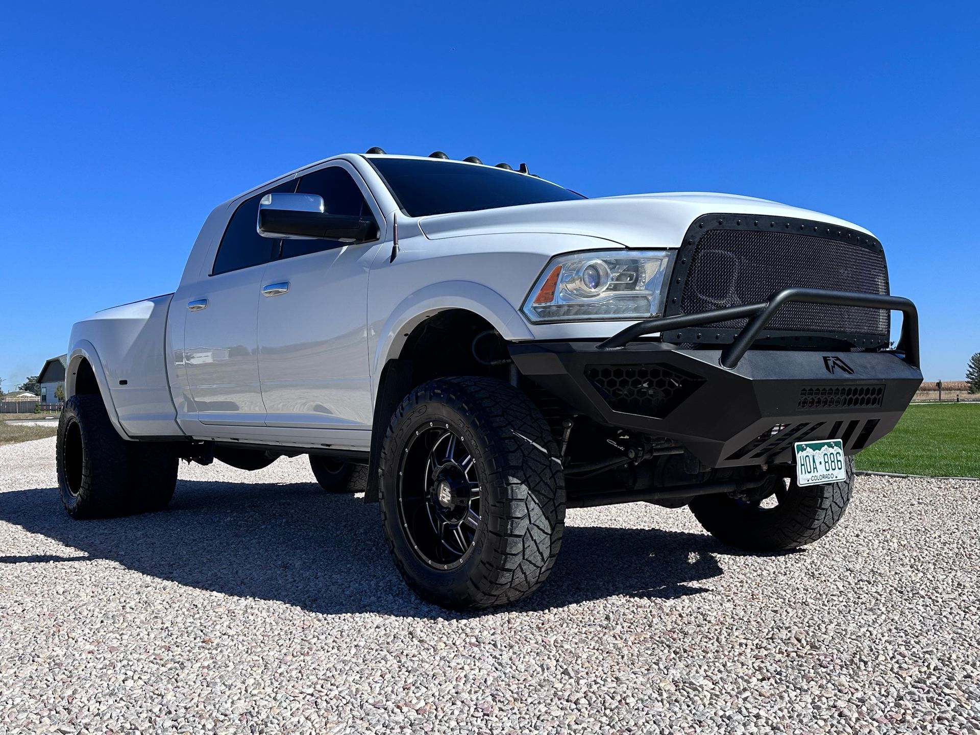 White lifted pickup truck on gravel, angled front view under a clear blue sky.