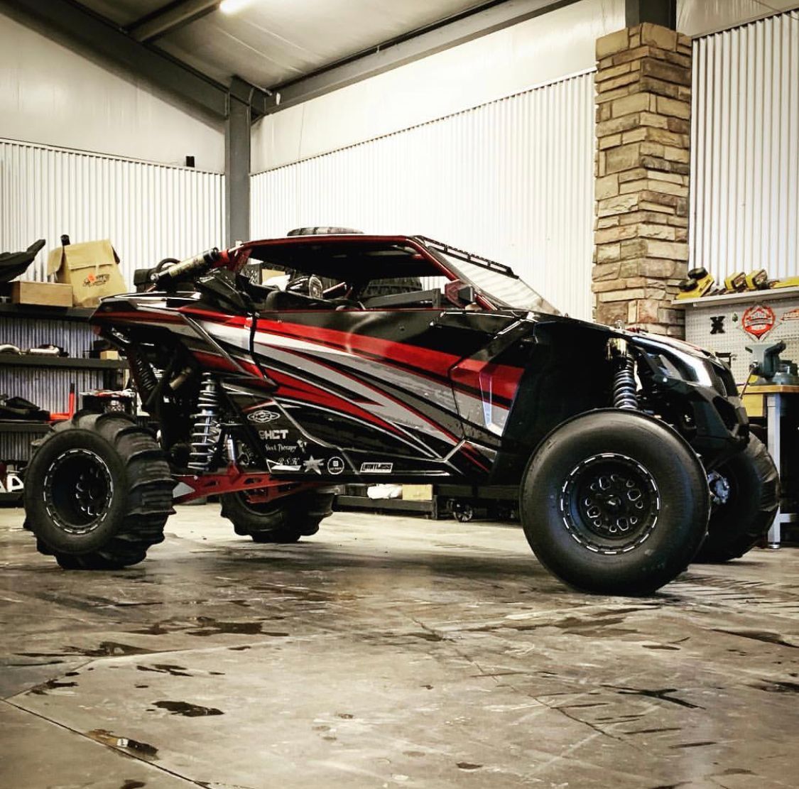 Lifted black and red off-road buggy in a garage, with large tires and a rugged custom body.