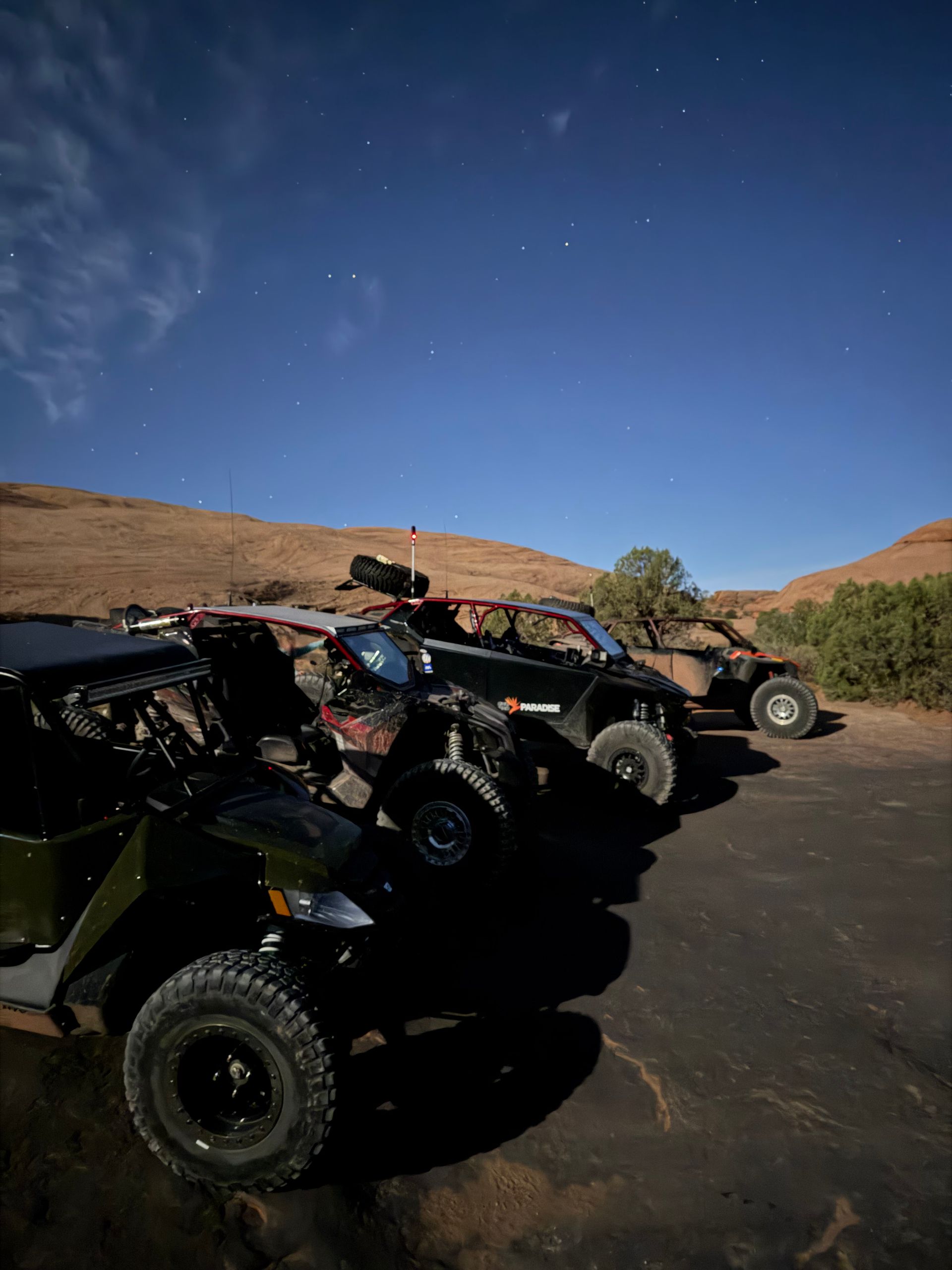 Off-road vehicles parked on a paved road beside dry hills under a clear blue sky