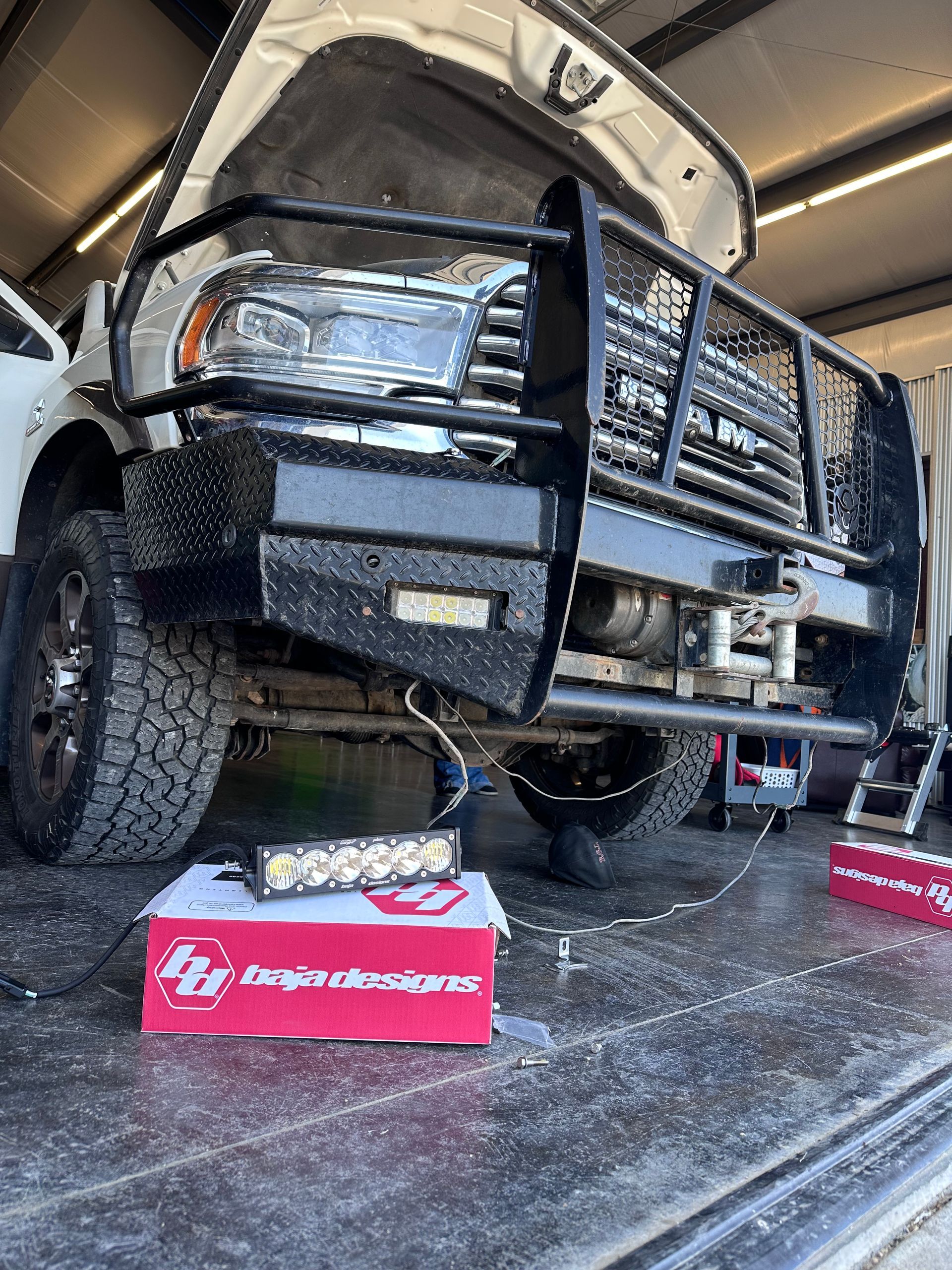 Off-road truck in a garage, front end lifted on ramps with tools on the floor.