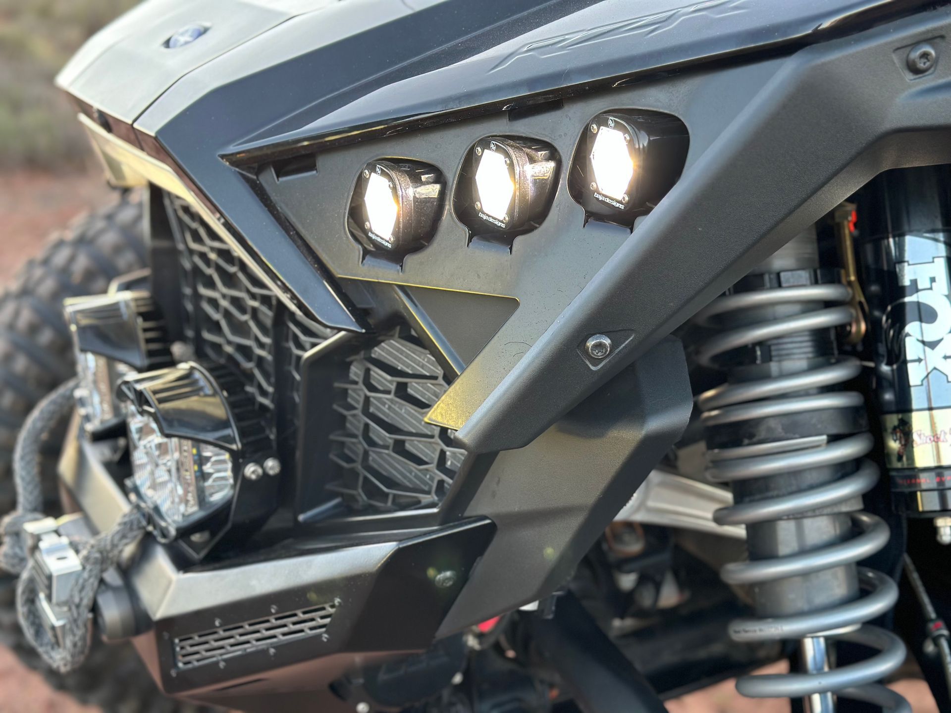 Close-up of a black off-road vehicle front with triple headlights and a visible coil spring suspension.