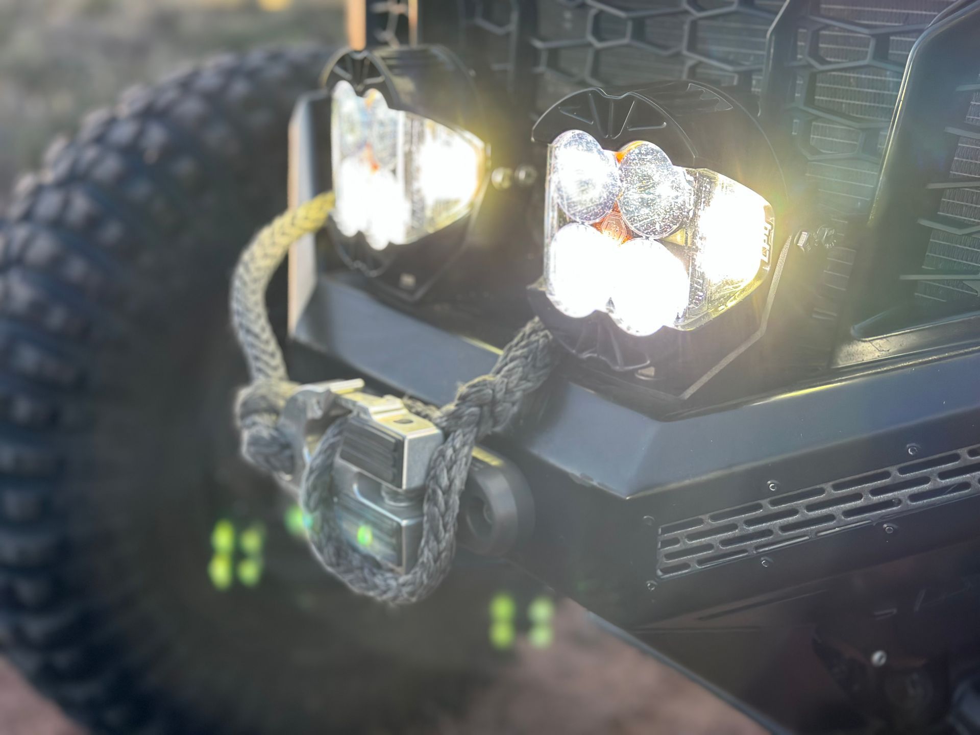 Close-up of an off-road vehicle’s front lights and bumper with a rope wrapped around the grille.